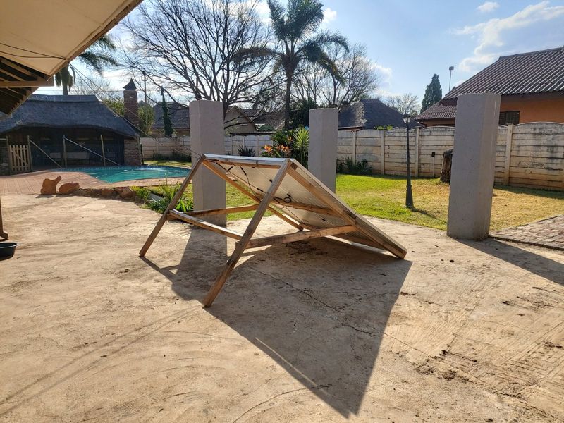 Rear garden area featuring a swimming pool, paved patio space, and concrete structural pillars, with a temporary solar panel setup on the patio.