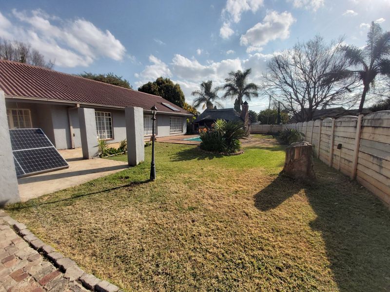 Rear garden featuring a swimming pool, paved patio area, solar panels, and a thatched lapa, enclosed by a precast concrete boundary wall.