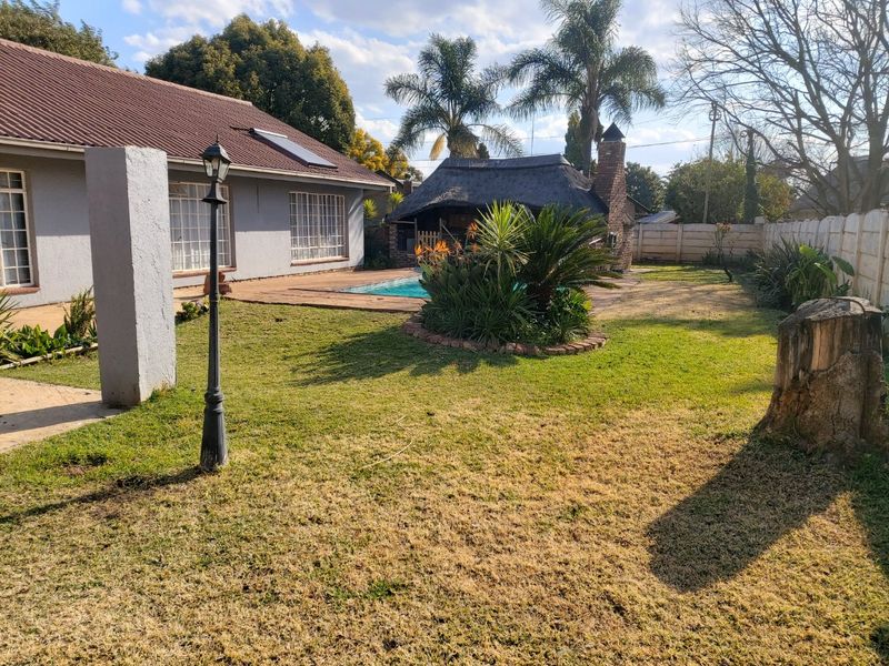 Rear garden featuring a swimming pool, a thatched lapa with a built-in fireplace, and established landscaping.