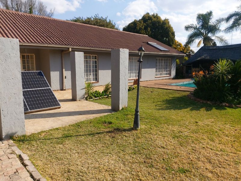 Rear exterior view featuring a tiled roof house, swimming pool, garden, and a thatched lapa area.