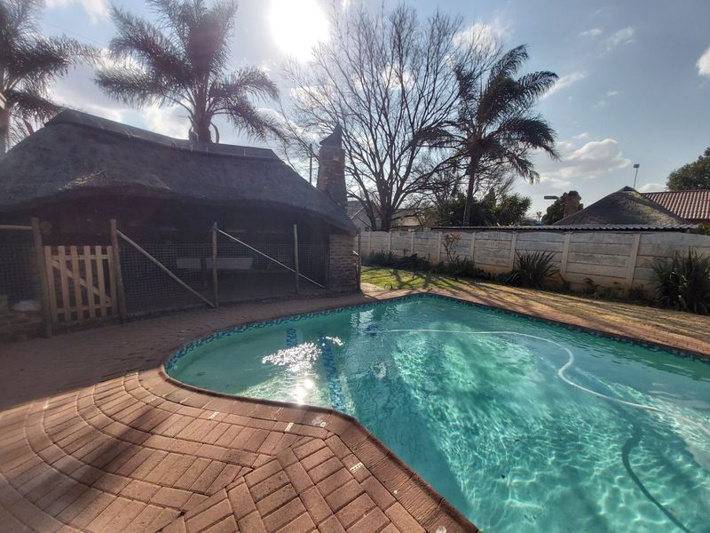 Outdoor pool area featuring a swimming pool, brick paving, and a traditional thatch roof lapa structure set within a private garden.