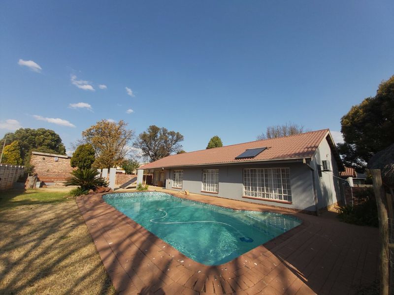 Rear exterior view featuring a swimming pool with solar heating, paved surround, and a single-story residence with a tiled roof.