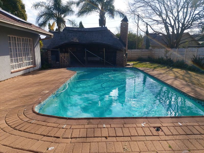Outdoor pool area featuring a swimming pool, brick paved surround, and a thatched lapa structure in the rear garden.
