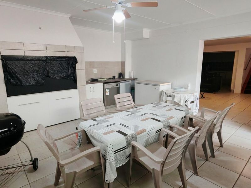 Covered patio area featuring a built-in braai, tiled flooring, and a ceiling fan, providing a functional space for outdoor dining and entertainment.