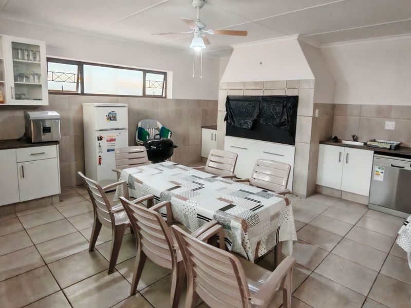 Spacious open-plan kitchen and dining area featuring built-in cabinetry, tiled flooring, and a built-in braai, offering a functional layout for entertaining.