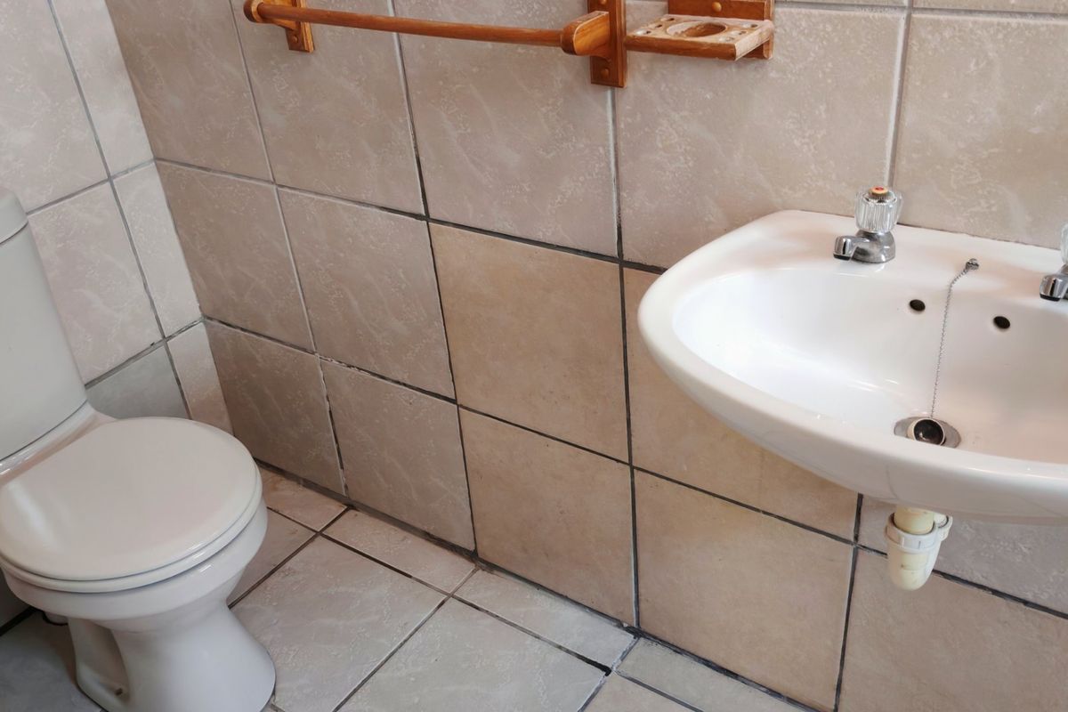 A compact bathroom featuring a wall-mounted basin, close-coupled toilet, and neutral ceramic tiling throughout.