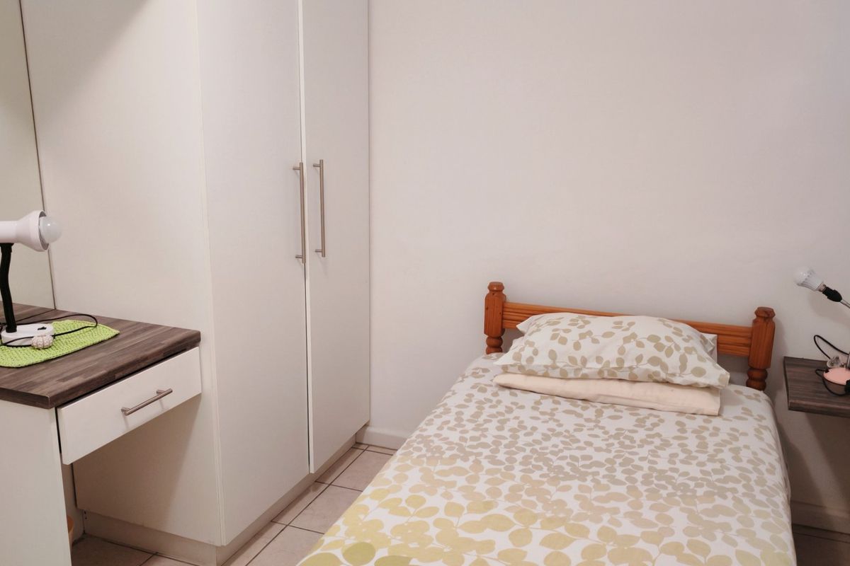 A compact bedroom featuring a built-in wardrobe, integrated vanity unit, and tiled flooring.