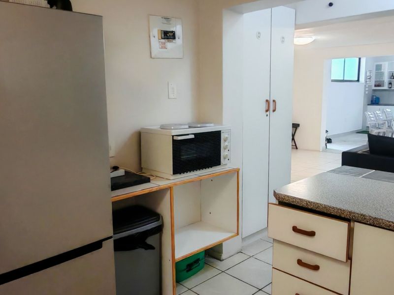 A functional kitchen area featuring tiled flooring, built-in cabinetry with laminate countertops, and a dedicated pantry cupboard, connecting to the adjacent living space.