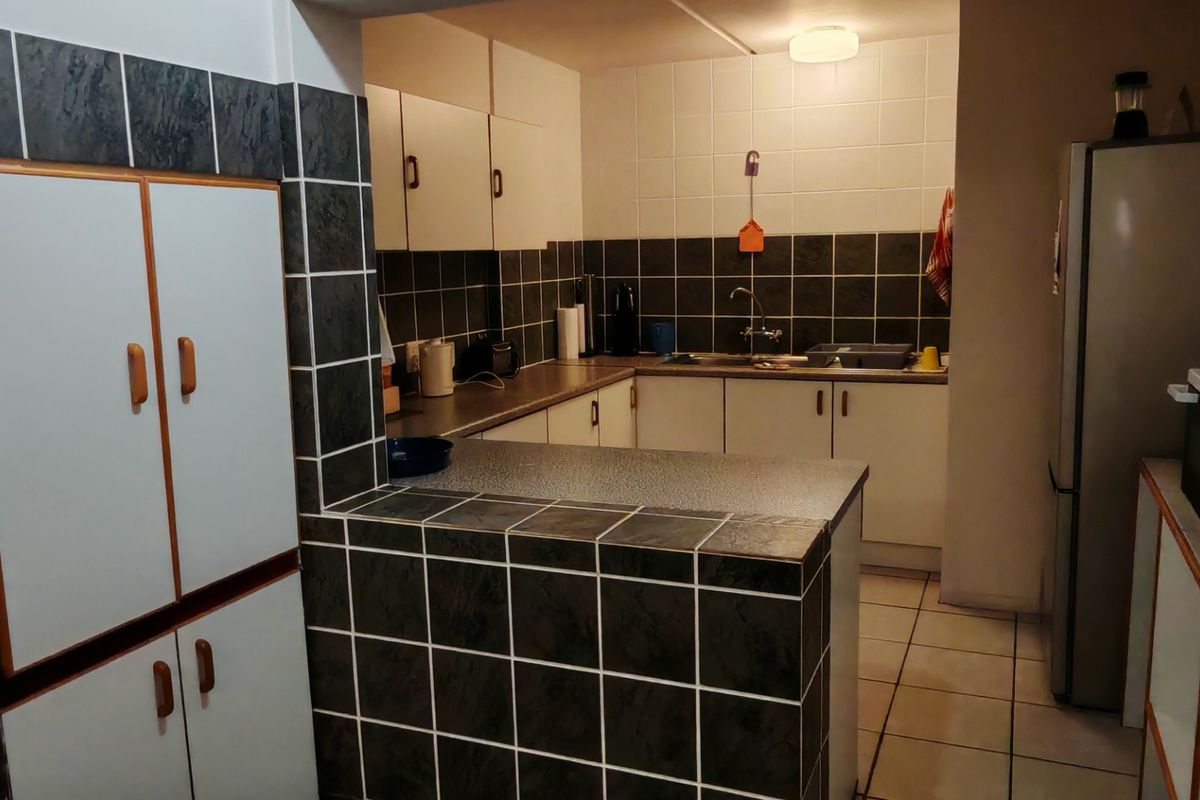 A functional kitchen featuring tiled splashbacks, laminate countertops, and built-in cabinetry, offering a dated aesthetic with potential for modern renovation.
