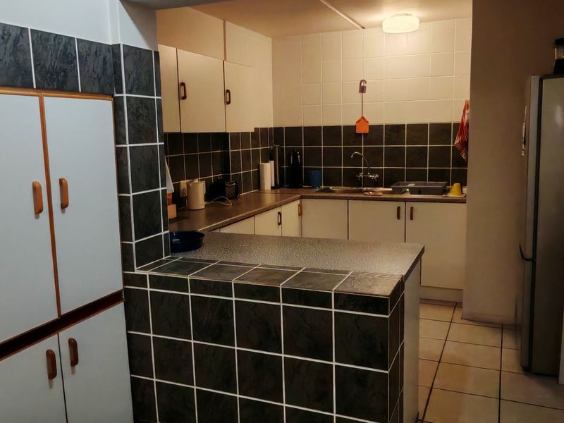 A functional kitchen featuring tiled splashbacks, laminate countertops, and built-in cabinetry, offering a dated aesthetic with potential for modern renovation.