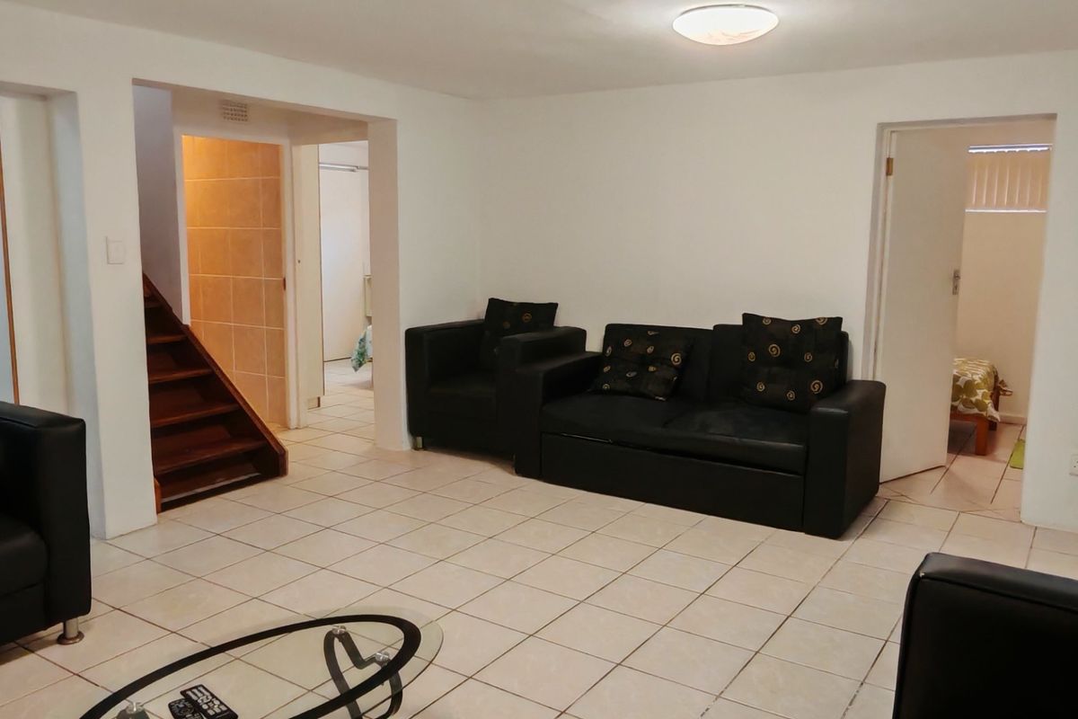 A living room featuring tiled flooring, a wooden staircase leading to an upper level, and built-in storage cupboards.