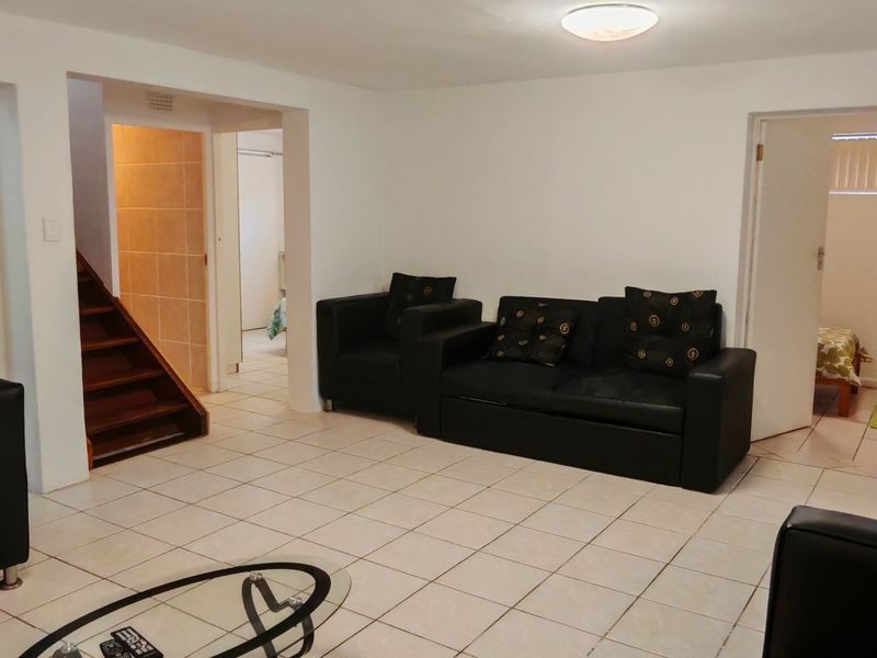 A living room featuring tiled flooring, a wooden staircase leading to an upper level, and built-in storage cupboards.