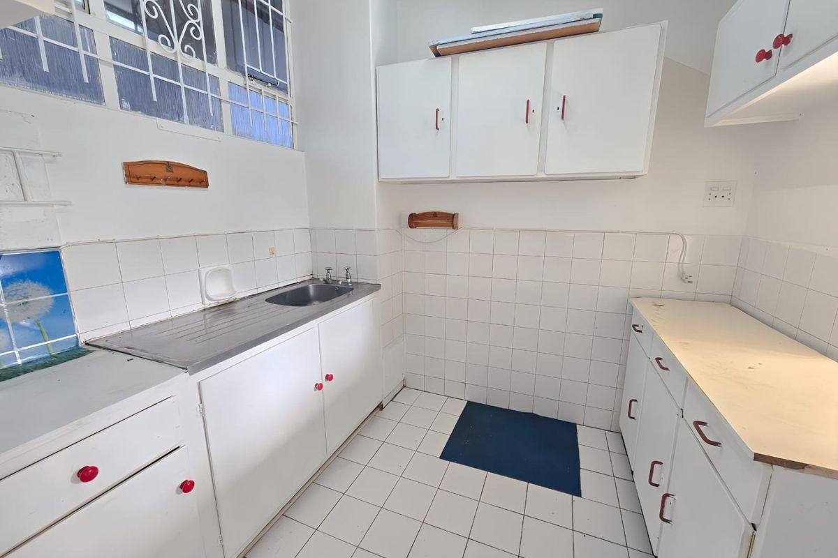 A functional kitchen space featuring white built-in cabinetry, a stainless steel sink, tiled splashbacks, and tiled flooring, ready for modernization.