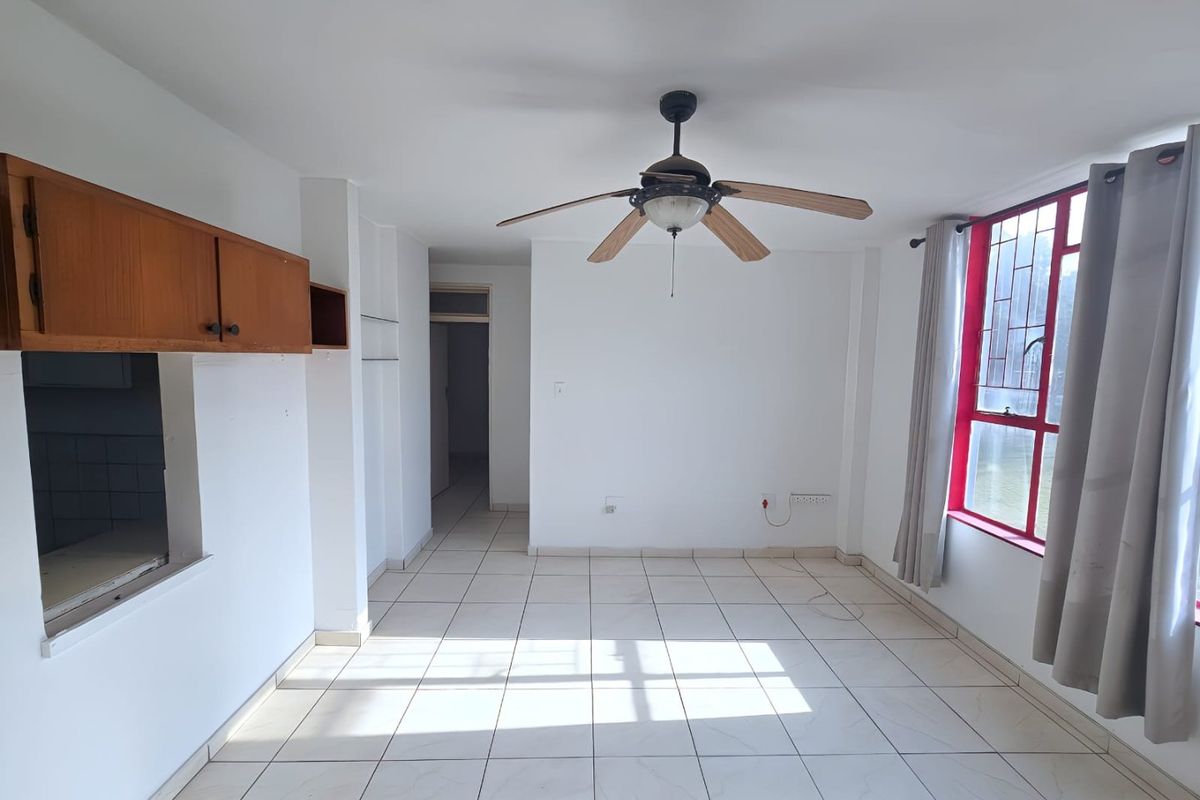 An empty living room featuring tiled flooring, a ceiling fan, and built-in wall cabinetry, with natural light entering through a large window.