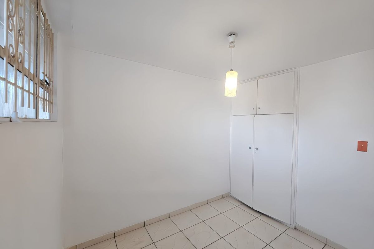 A clean, empty bedroom featuring tiled flooring, a built-in wardrobe, and a window with security bars.