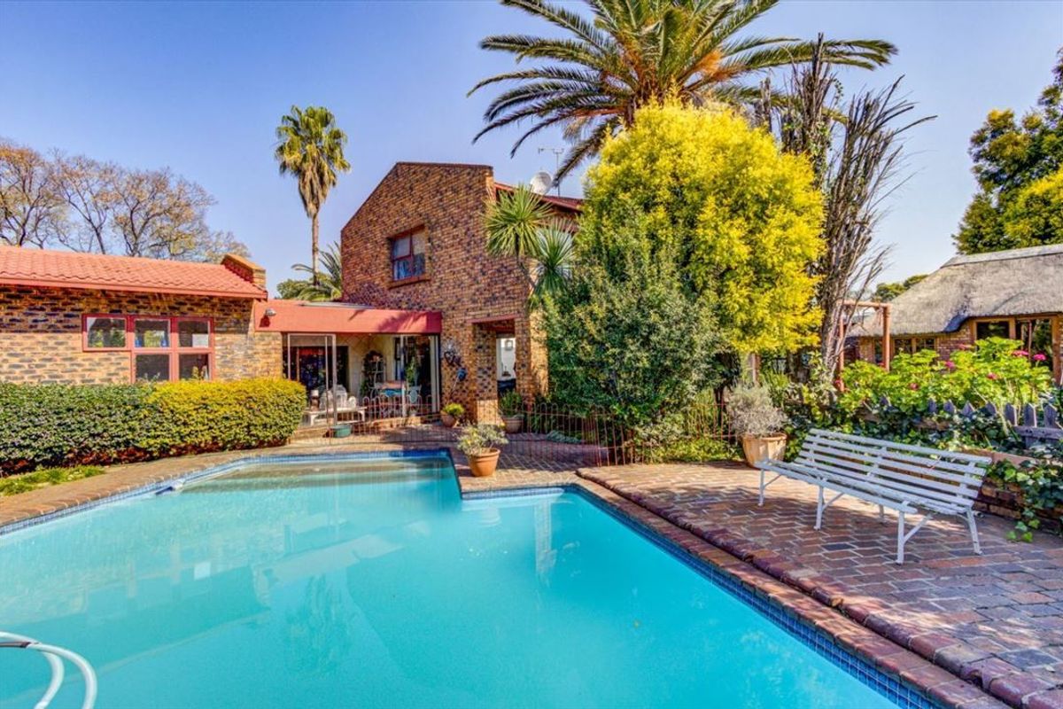 A well-maintained outdoor pool area featuring a swimming pool, brick paving, and a classic face brick house facade with mature garden landscaping.
