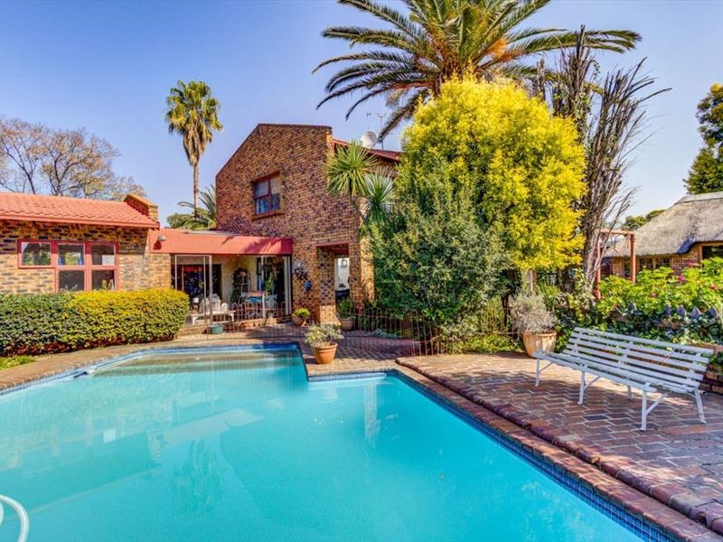 A well-maintained outdoor pool area featuring a swimming pool, brick paving, and a classic face brick house facade with mature garden landscaping.