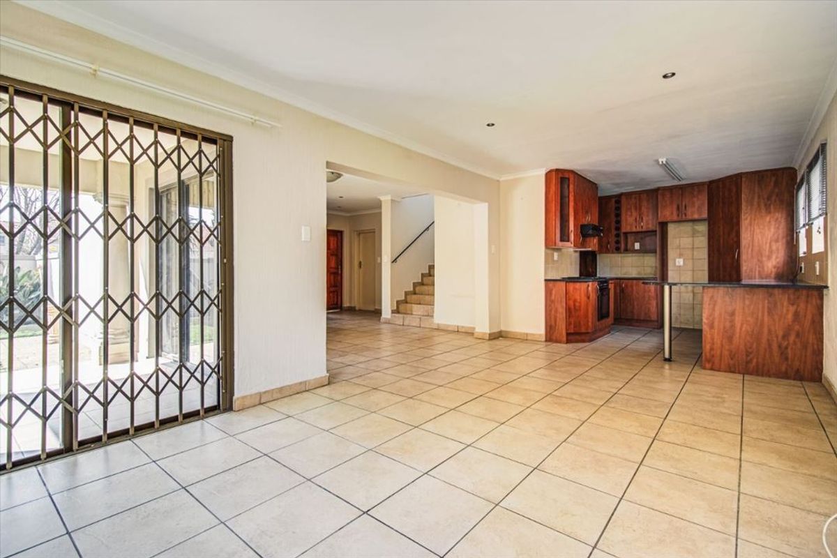 Spacious open-plan living area featuring tiled floors, a functional kitchen with built-in cabinetry, and direct access to the outdoor patio through a security gate.