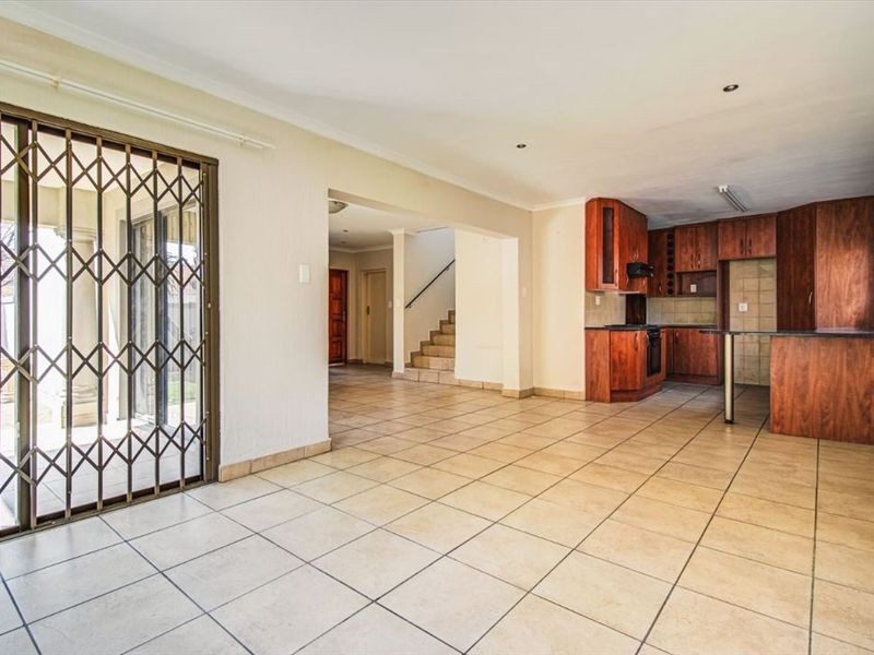 Spacious open-plan living area featuring tiled floors, a functional kitchen with built-in cabinetry, and direct access to the outdoor patio through a security gate.