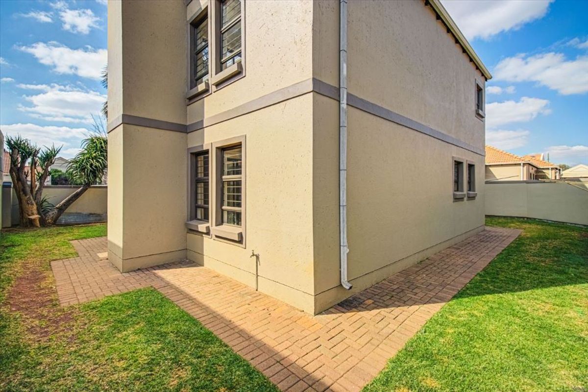 Side view of the townhouse exterior featuring a paved walkway, plastered facade, and a small garden area with boundary walling.