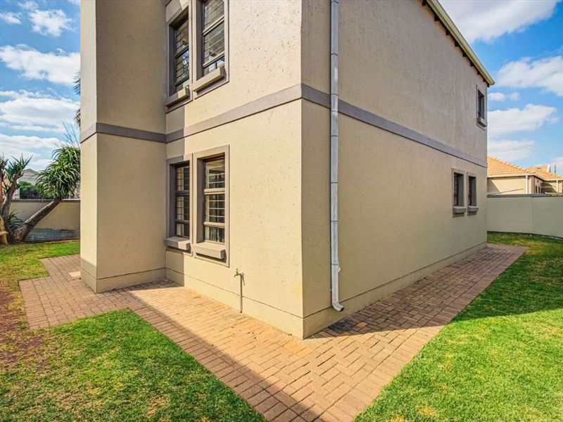 Side view of the townhouse exterior featuring a paved walkway, plastered facade, and a small garden area with boundary walling.