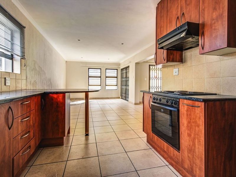 Open-plan kitchen and living area featuring wood-finish cabinetry, granite countertops, built-in oven, and tiled flooring throughout.