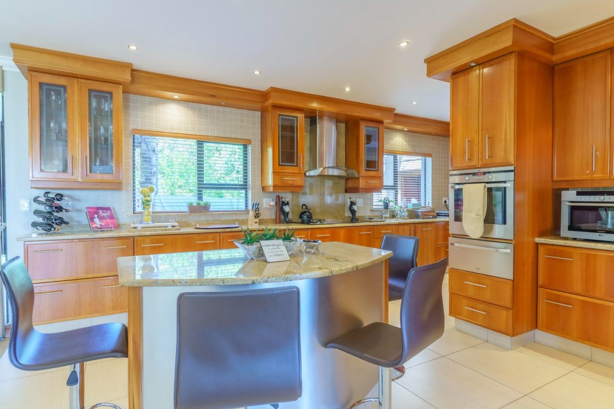 A well-maintained kitchen featuring warm wood cabinetry, granite countertops, a central island with breakfast bar seating, and built-in stainless steel appliances.