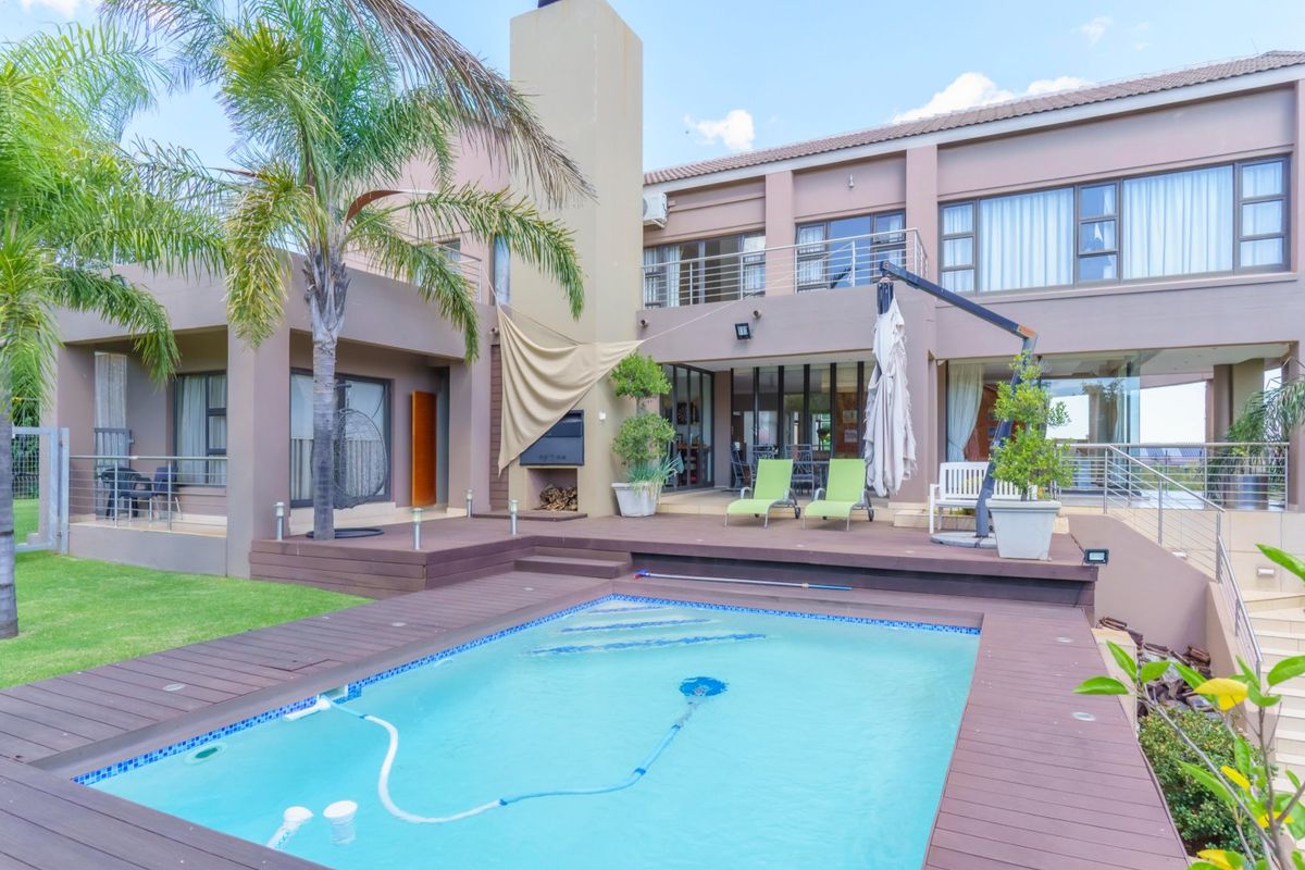 A spacious rear exterior featuring a swimming pool, timber decking, built-in fireplace, and a multi-level facade with balcony access.