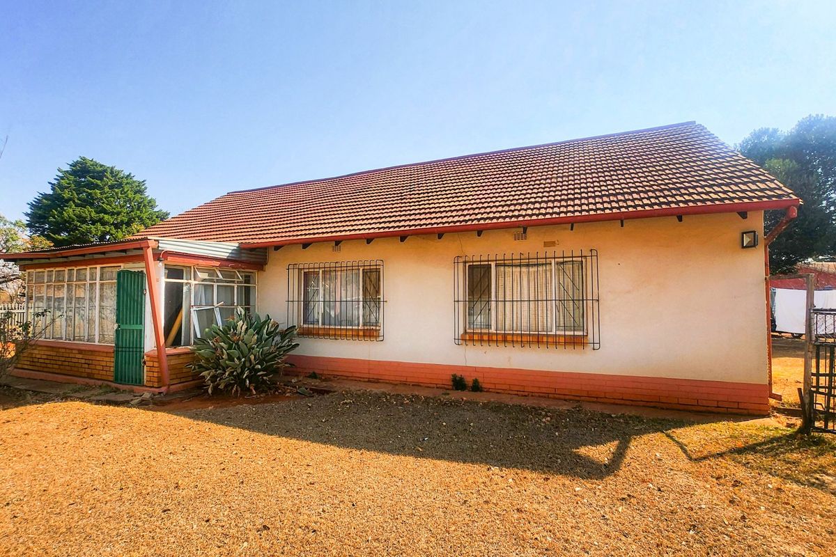 Rear view of a single-story house featuring a tiled roof, security bars on windows, and an enclosed patio area with a metal gate.