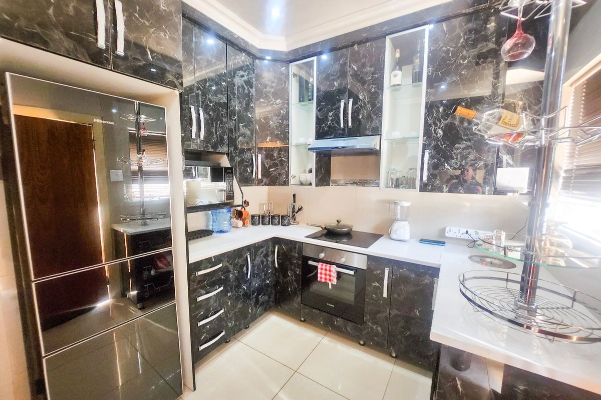 Modern kitchen featuring high-gloss marble-effect cabinetry, stone countertops, built-in oven, electric hob, and sleek tiled flooring.