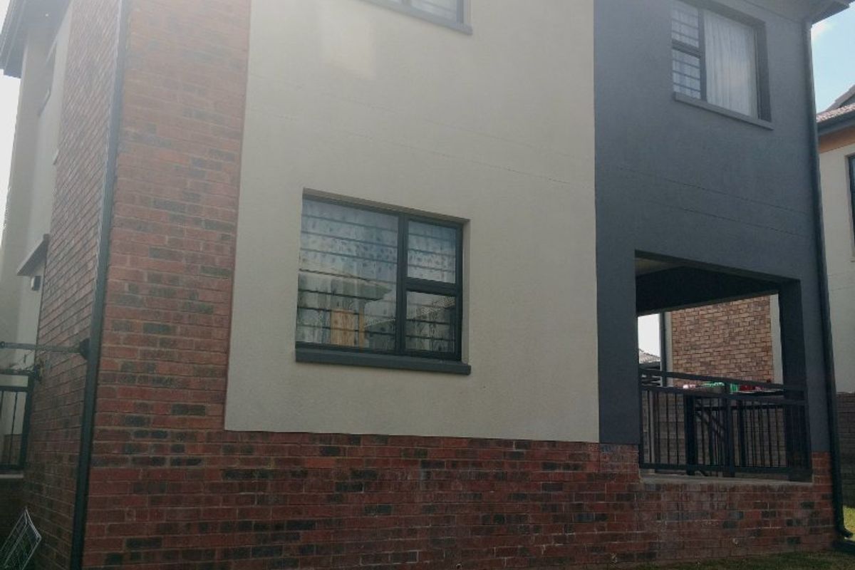 Rear view of a modern two-story house featuring a combination of brick and plastered finishes, aluminium windows, and a covered patio area.