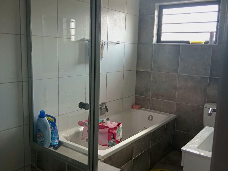 A functional bathroom featuring a built-in bathtub, separate glass-enclosed shower, and a vanity basin with neutral tiled finishes.