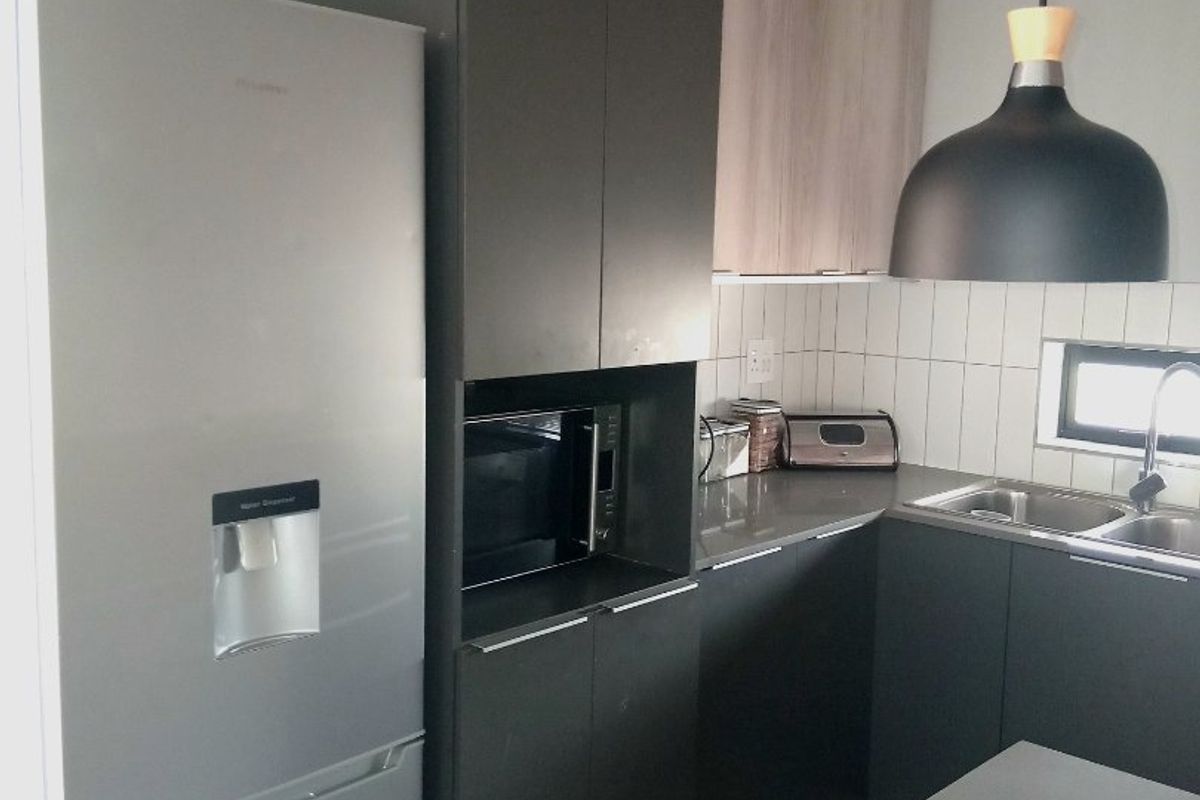 Modern kitchen featuring dark cabinetry, stone countertops, a double sink, and integrated microwave, complemented by stylish pendant lighting and a tiled backsplash.