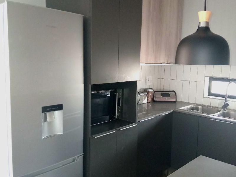 Modern kitchen featuring dark cabinetry, stone countertops, a double sink, and integrated microwave, complemented by stylish pendant lighting and a tiled backsplash.