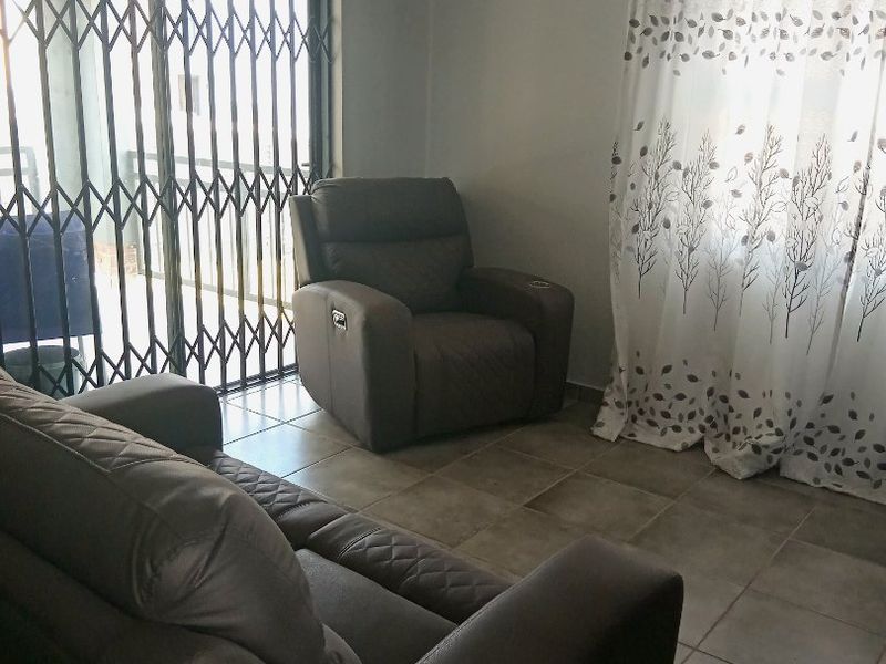 A living room area featuring tiled flooring and a sliding door with a security gate, providing access to the outdoor space.