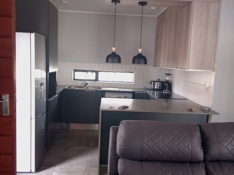 Modern open-plan kitchen featuring sleek cabinetry, a functional island, tiled flooring, and contemporary pendant lighting, seamlessly integrated into the living space.