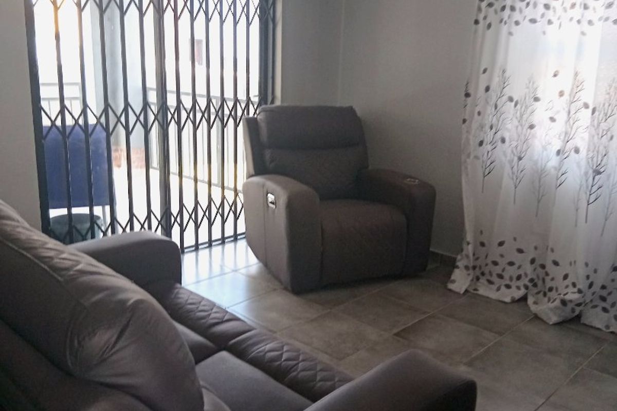 A living room featuring tiled flooring and a sliding door with a security gate, providing access to the exterior.
