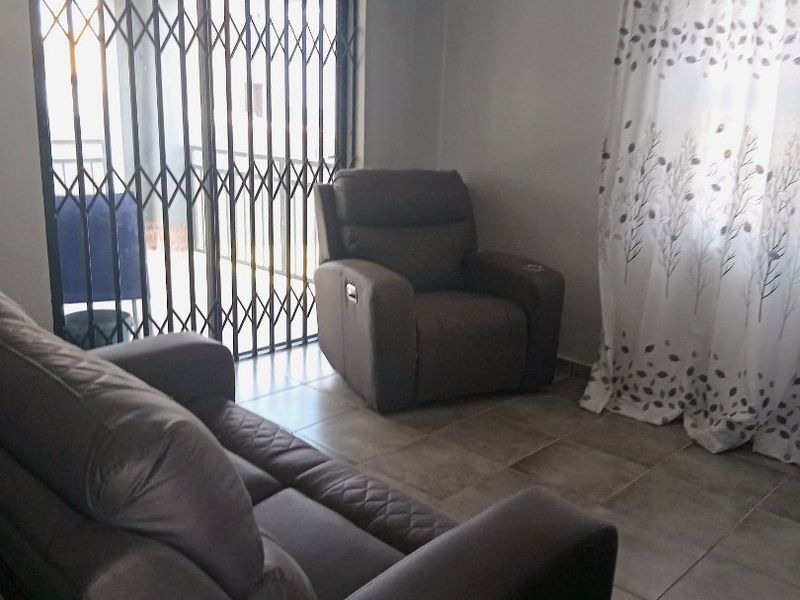 A living room featuring tiled flooring and a sliding door with a security gate, providing access to the exterior.