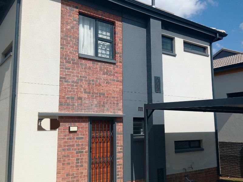 Front elevation of a modern two-story house featuring a brick and plaster facade, a metal security gate, and an attached carport with paved driveway.