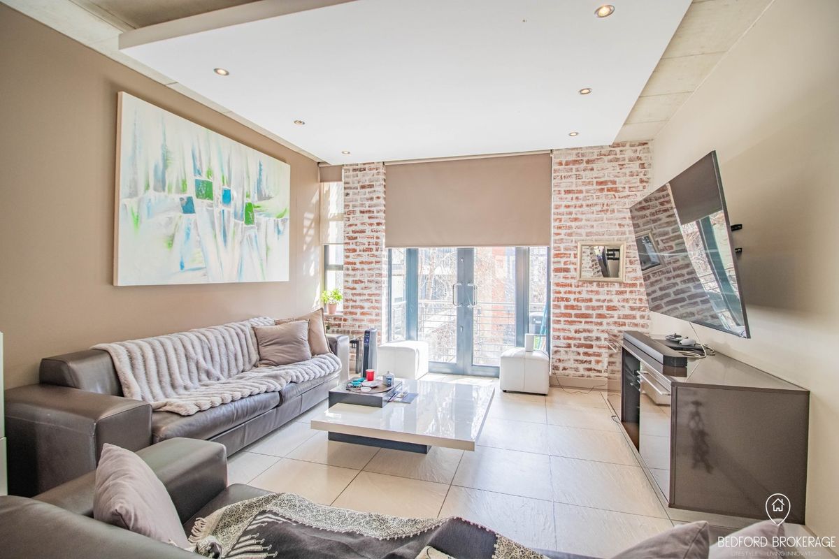 Modern living room featuring an exposed brick wall, tiled flooring, recessed ceiling lights, and double glass doors leading to an outdoor area.