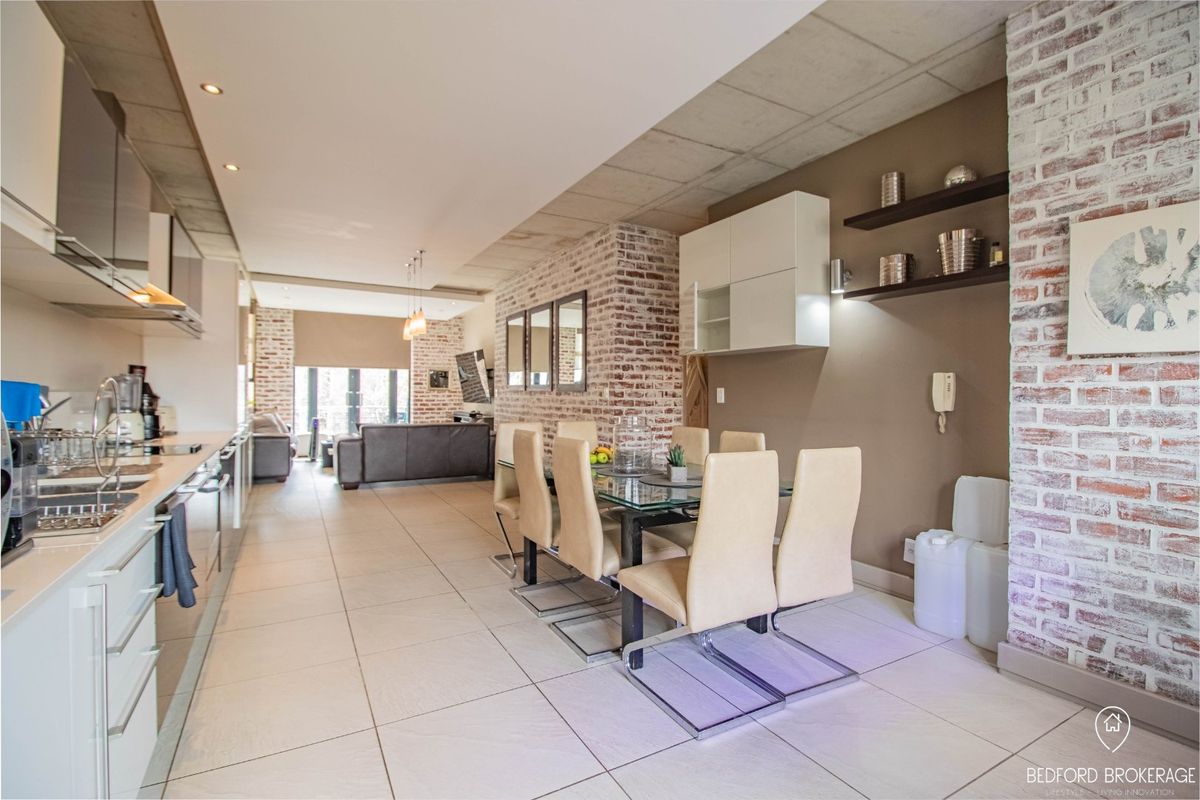 Spacious open-plan living and dining area featuring exposed brick accents, modern cabinetry, and sleek tiled flooring, creating a contemporary industrial aesthetic.