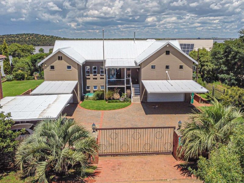 Aerial view of a large residential property featuring a metal roof, paved driveway, security gate, carport, solar panels, and a swimming pool.