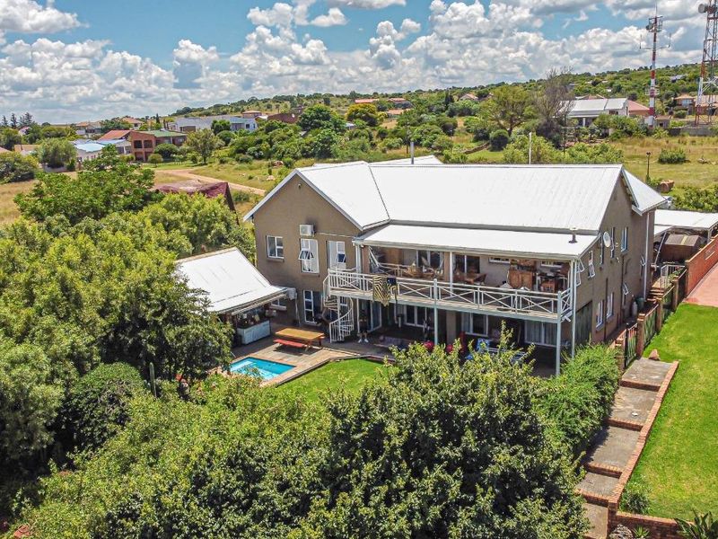 Aerial view of a multi-story residential property featuring a swimming pool, expansive garden, and a large balcony with a spiral staircase.