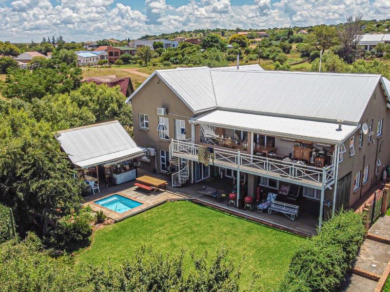 Aerial view of a multi-story house featuring a swimming pool, wooden decking, a covered patio, and a balcony with a spiral staircase.