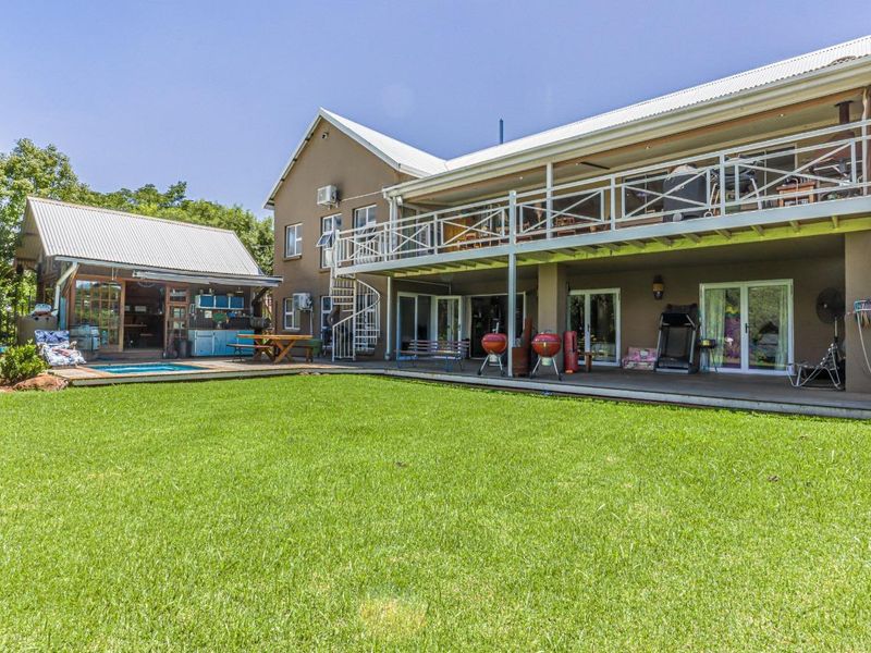 Rear view of the property featuring a large lawn, swimming pool, covered patio, and an upper-level balcony with a spiral staircase.