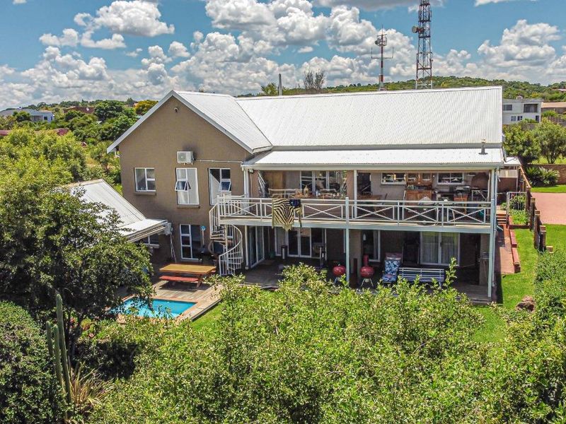 Aerial view of the rear elevation featuring a raised wooden deck, spiral staircase, swimming pool, and a large corrugated metal roof.