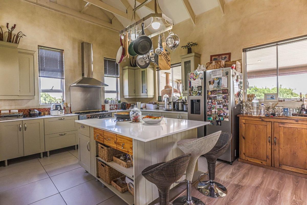 Spacious kitchen featuring a central island with stone countertops, vaulted ceilings with exposed beams, and ample built-in cabinetry with a stainless steel extractor fan.