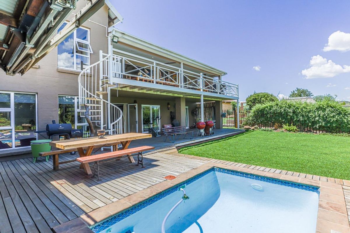 Rear exterior view featuring a raised wooden deck, a spiral staircase connecting to the upper balcony, and a swimming pool set in a garden.