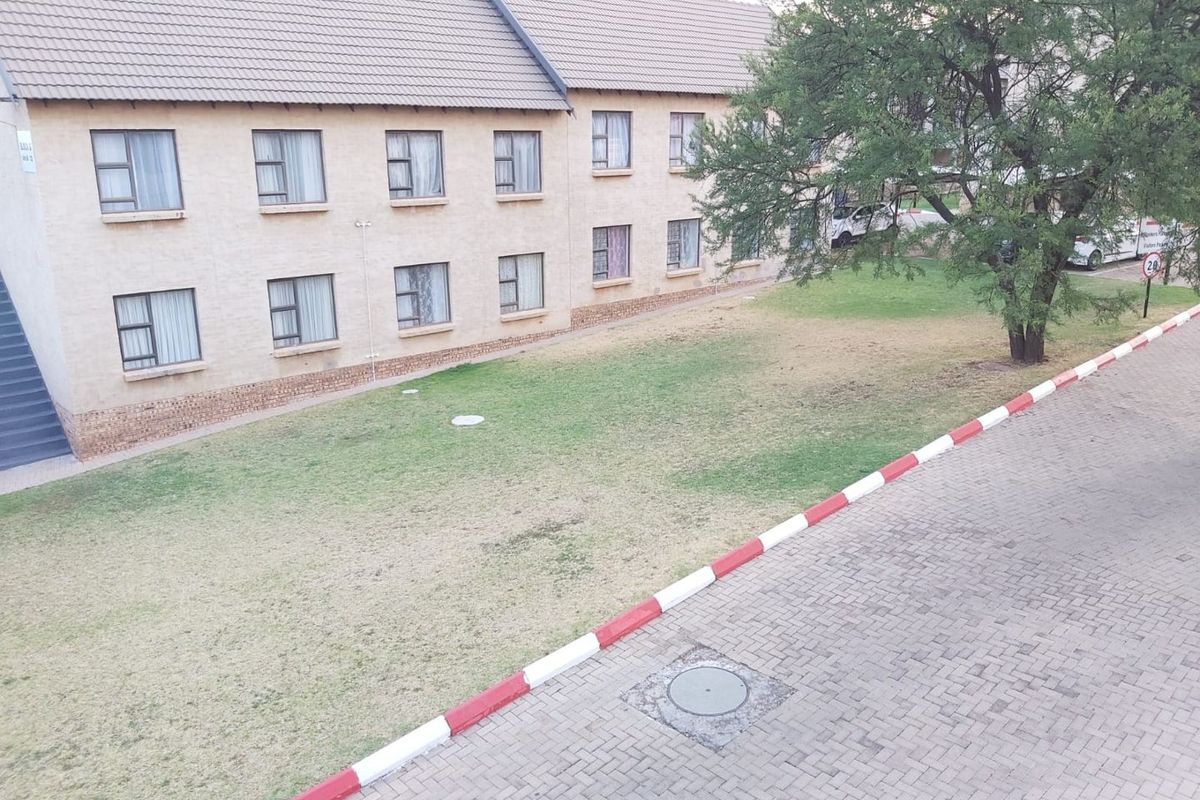 An elevated view of an apartment complex exterior featuring a paved driveway, communal lawn area, and multi-story residential building with tiled roofing.