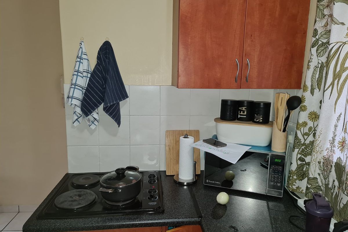 A compact kitchen corner featuring a built-in electric hob, dark laminate countertops, and wooden cabinetry with a tiled splashback.